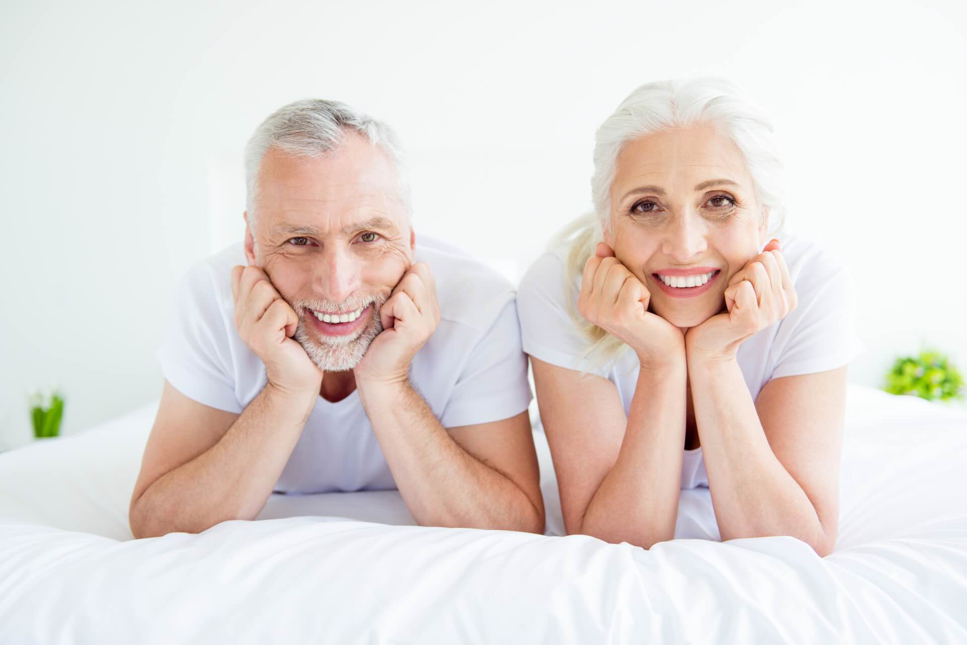 Make break or pause, feel happiness! Close up portrait of two grey hair people, stay at house on holiday lie on linen, sheets, soft couch look at the camera next to each other
